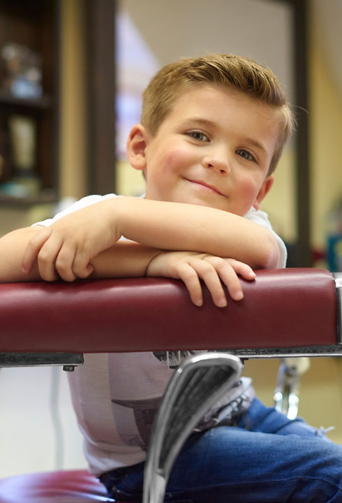 A boy smiling in the barber chair after a haircut